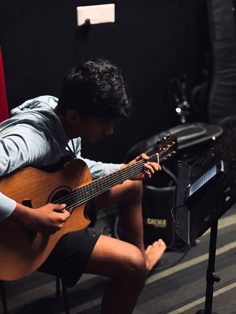 A SARA Music School student playing acoustic guitar with sheet music